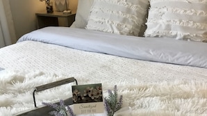 Un lit bien fait, avec du linge de lit blanc, un plateau avec des serviettes et une carte, et une lampe sur une table de chevet.