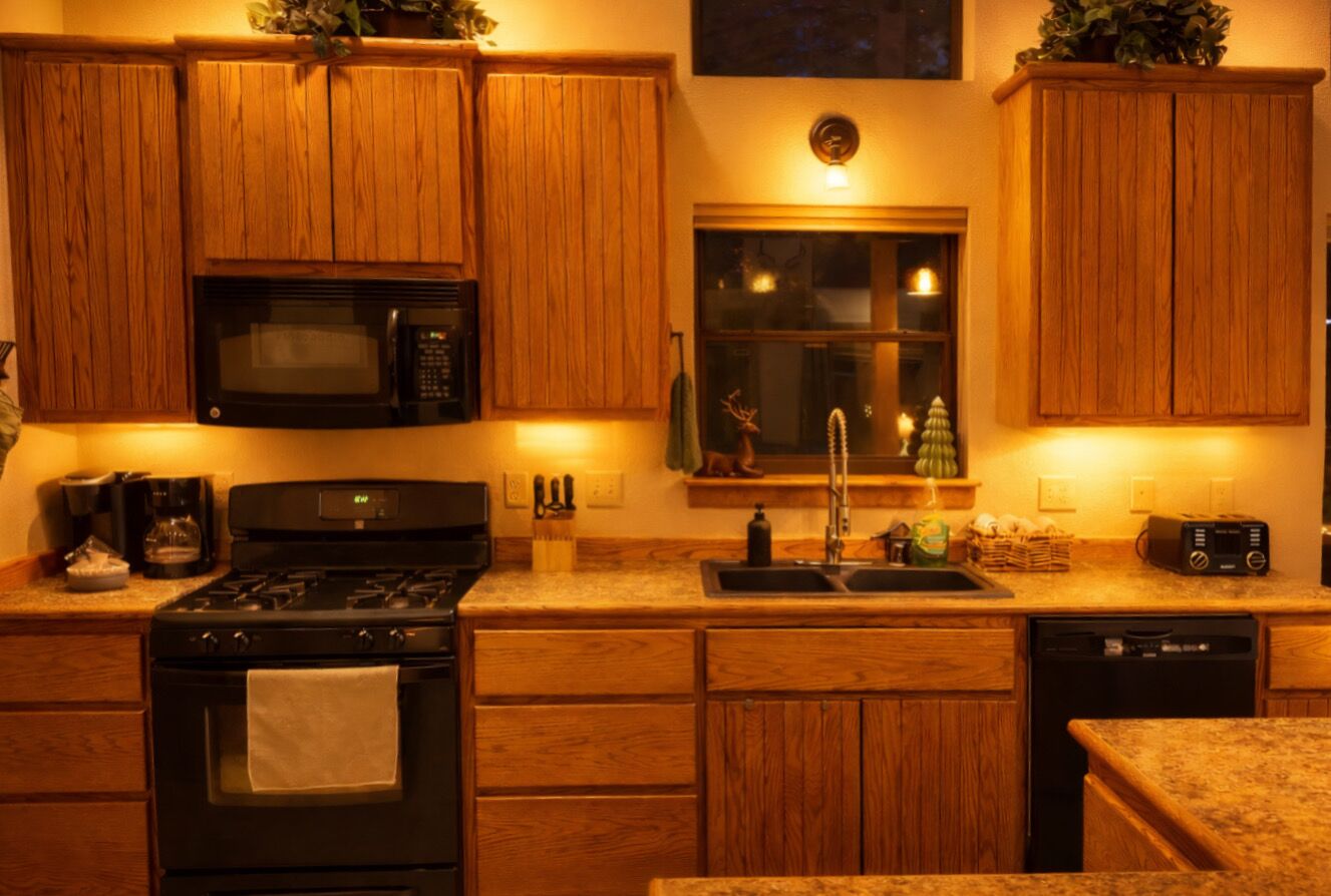 Une cuisine avec des meubles de rangement en bois, un four à micro-ondes, une cuisinière, un évier et un lave-vaisselle.