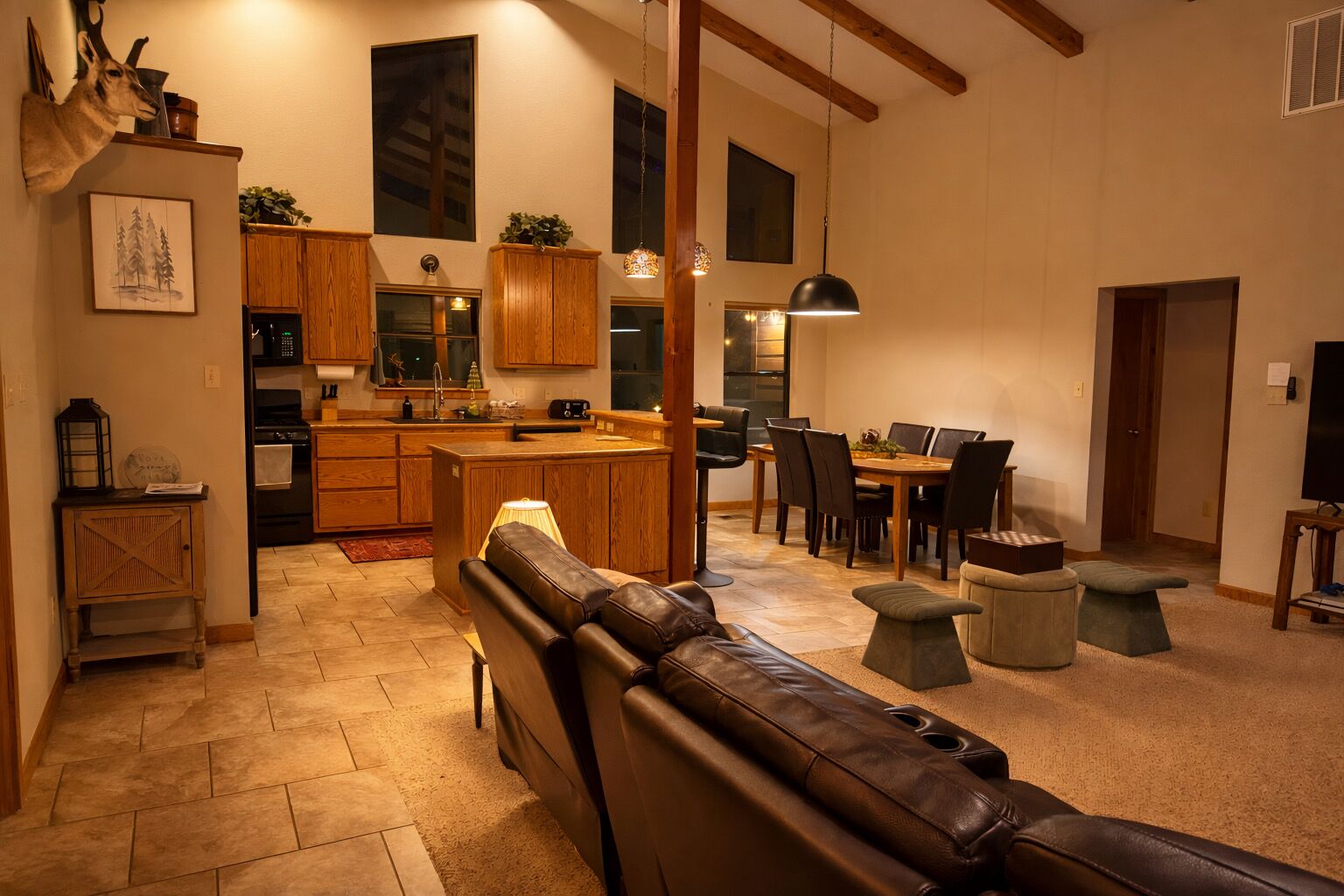 A spacious living area with a leather sofa, a dining table with chairs, a kitchen with wooden cabinets, and a large window.