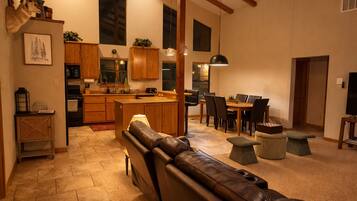 A spacious living area with a leather sofa, a dining table with chairs, a kitchen with wooden cabinets, and a large window.