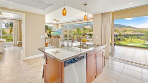 A modern kitchen with a large island, a built-in dishwasher, and a view of a lush landscape. - Maui Resort Rentals: Honua Kai - 4 Total Bedrooms, Gorgeous West Maui Mountain & Partial Ocean Views! (Lahaina)