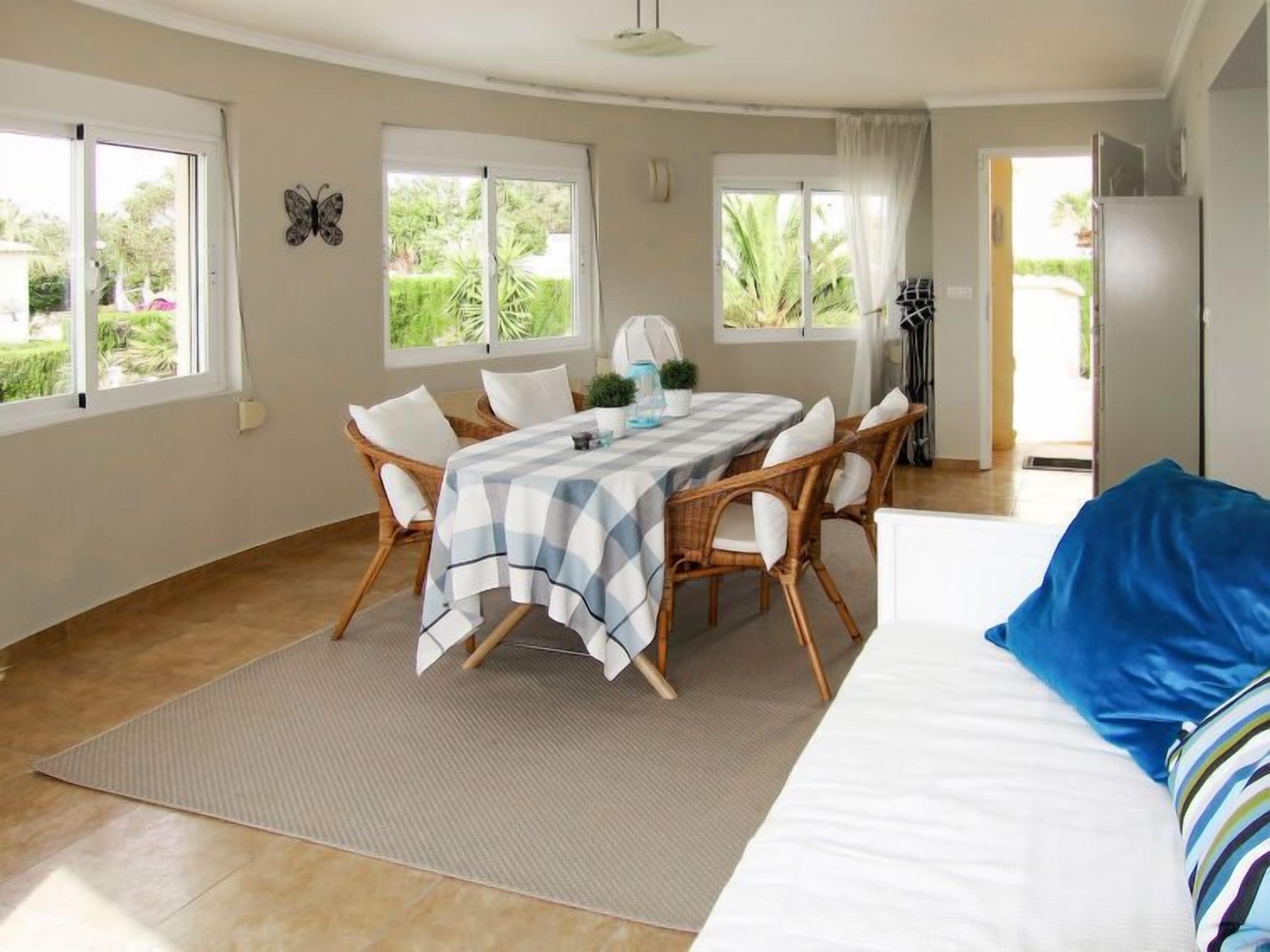 A room with a dining table, chairs, a bed, and a view of greenery outside.