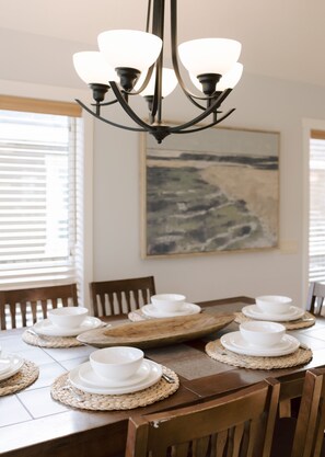 A dining table set with white bowls and plates, a woven placemat, and a chandelier.