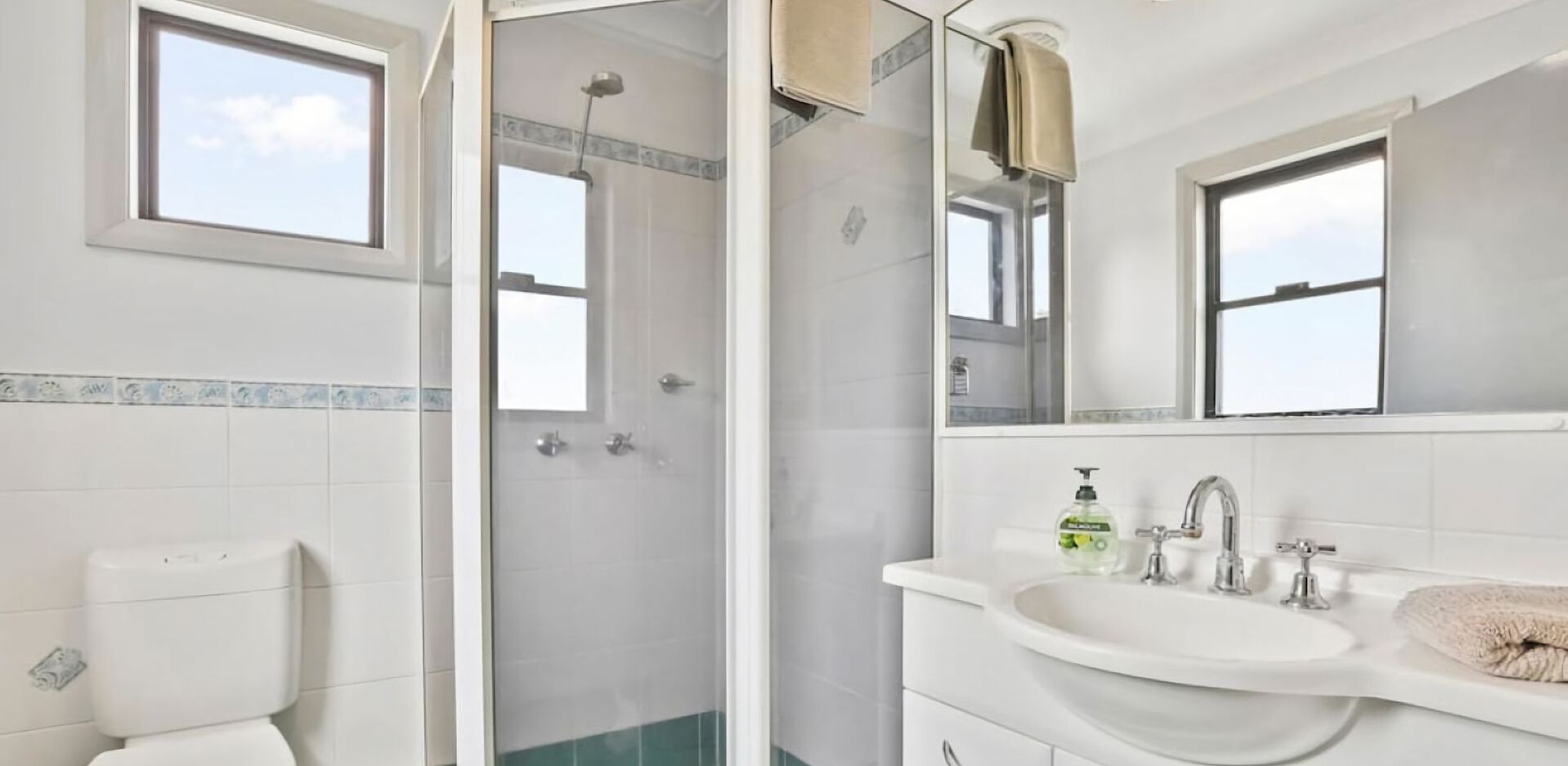 Un bany modern amb plat de dutxa de vidre, un vàter, un lavabo amb una tovallola i un mirall.