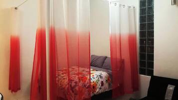 A bedroom with a bed, a red and white shower curtain, and a tiled floor.