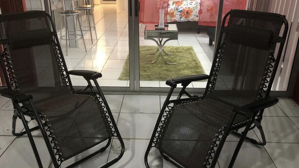 Ein Balkon mit zwei schwarzen Netzkufen, einer Glastür und Blick auf einen Essbereich mit Stühlen und einem Tisch.