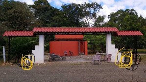 Ein pavillonrotes Pavillon mit weißem Unterbau, umgeben von Grünpflanzen und Außenbestuhlung.