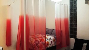 Ein Schlafzimmer mit einem Bett, das mit einem blumigen Bettbezug und einem grauen Kissen sowie einem roten und weißen Baldachin ausgestattet ist.