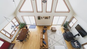 Een ruime loft met hoge plafonds, grote ramen, een houten eettafel, een bank, een televisie en een open haard.