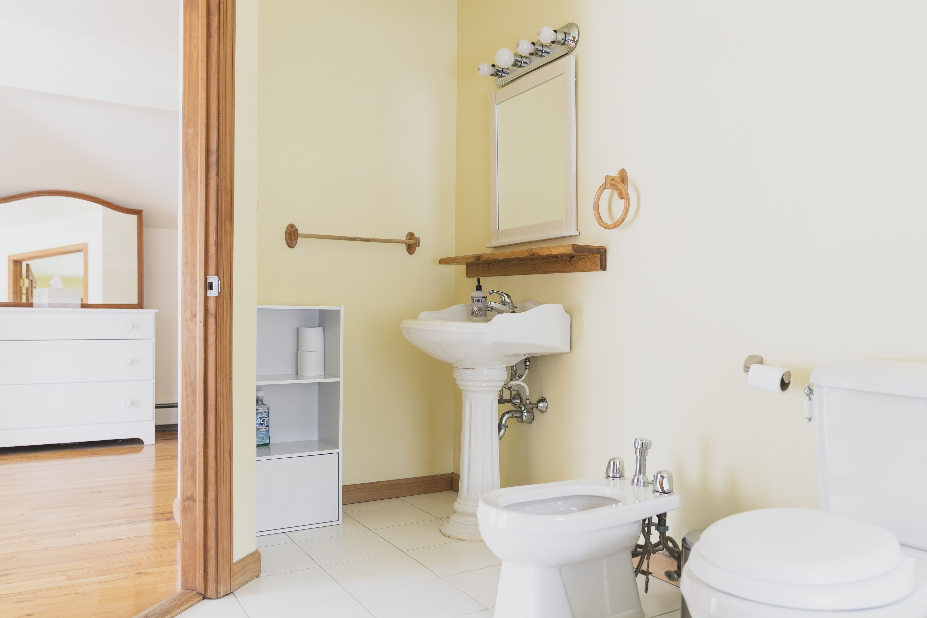 A bathroom with a white sink, mirror, and toilet. There is a wooden door frame and a shelf with toiletries.
