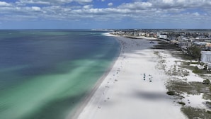 Una playa costera con vista clara al océano, orilla arenosa y edificios cercanos.