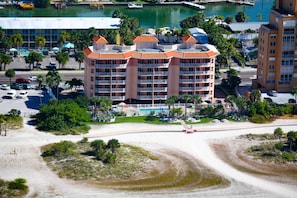 A multi-story hotel with a central courtyard, surrounded by parking and a beach area.
