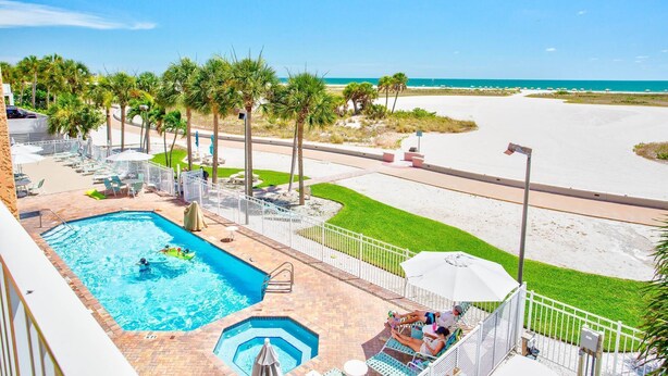 Un área de piscina con vista a la playa, un sendero vallado y una piscina pequeña.