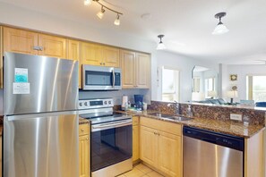A modern kitchen with stainless steel appliances, wooden cabinets, granite countertops, and pendant lighting.