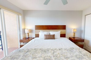 A hotel room with a large bed, two bedside tables with lamps, a wooden headboard, and a balcony door. - Beachfront Condo. Heated Pool. Activities, Fun, End Unit, Parking, & Great Location! (Treasure Island)