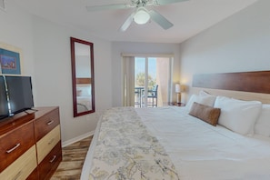A hotel room with a bed, a TV, a dresser, a ceiling fan, and a balcony with a table and chairs.