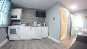 Una cocina compacta con electrodomésticos blancos, un televisor de pantalla plana y piso de madera.