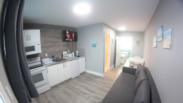 Una cocina moderna con electrodomésticos blancos, un televisor de pantalla plana y un comedor con sofá gris.