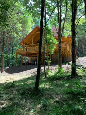Een houten hut met een overdekte veranda, omgeven door bomen.