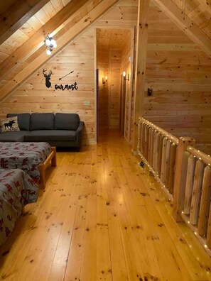 A cozy attic bedroom with wooden walls, a sofa, two beds, and a staircase leading to another room. - NEWER cabin, 5 BR, 2 fireplaces, hot tub, privacy (Logan)