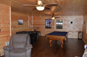 A cozy room with wooden walls, a pool table, a foosball table, and a reclining chair. - NEWER cabin, 5 BR, 2 fireplaces, hot tub, privacy (Logan)