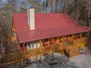 A cabin with a red metal roof, wooden deck, and a stone chimney. - NEWER cabin, 5 BR, 2 fireplaces, hot tub, privacy (Logan)