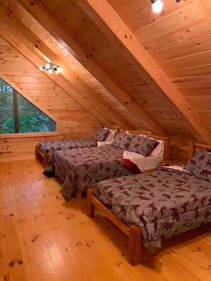A cozy attic bedroom with two beds, wooden floors, and a large window overlooking greenery. - NEWER cabin, 5 BR, 2 fireplaces, hot tub, privacy (Logan)