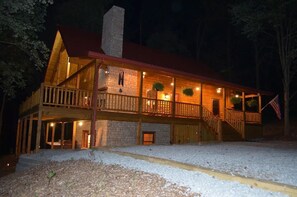 A two-story log cabin with a balcony, a stone chimney, and an American flag. - NEWER cabin, 5 BR, 2 fireplaces, hot tub, privacy (Logan)