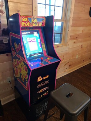 A Mr. Pac-Man arcade machine with a pink and blue design, placed next to a wooden floor and a window. - NEWER cabin, 5 BR, 2 fireplaces, hot tub, privacy (Logan)