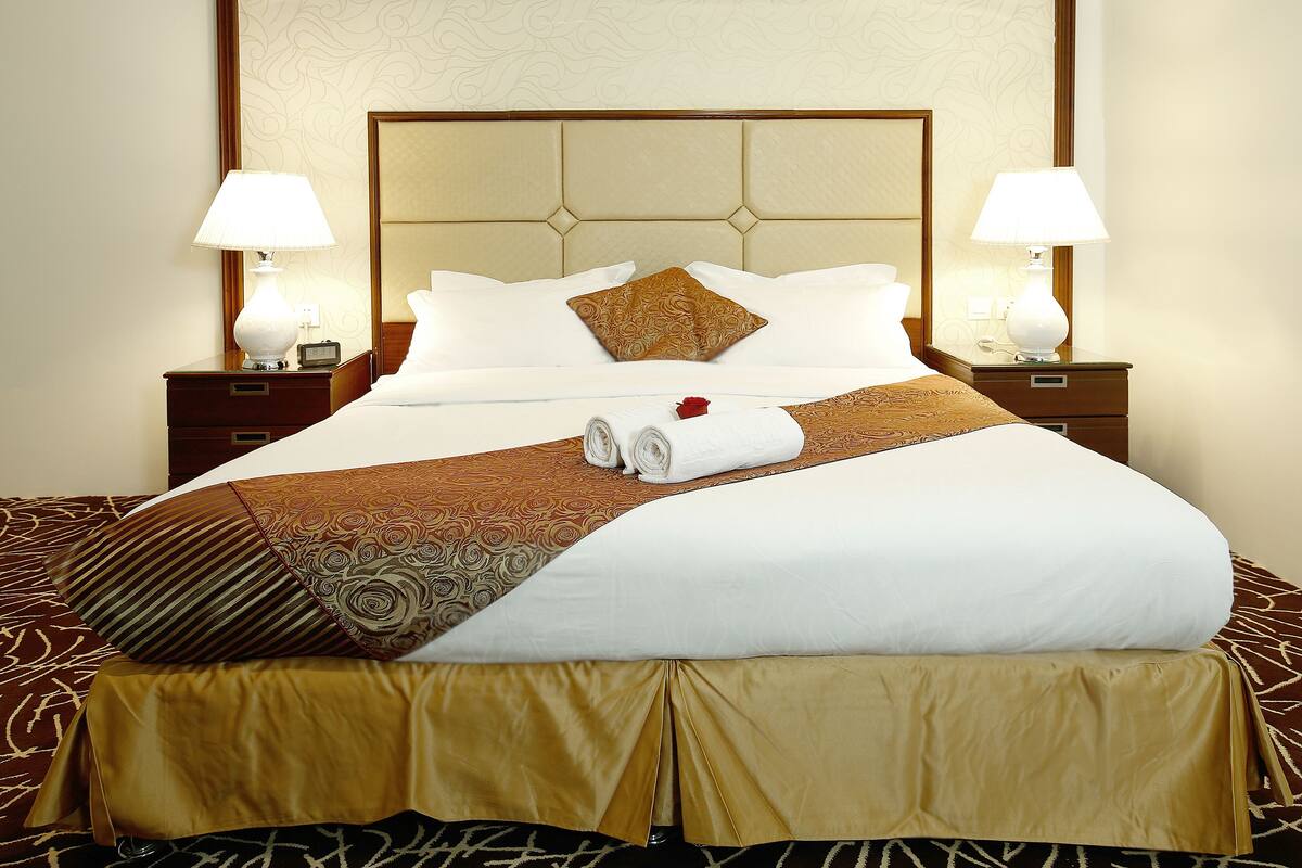 A neatly made bed with a patterned bedspread, two bedside lamps, and a decorative headboard.