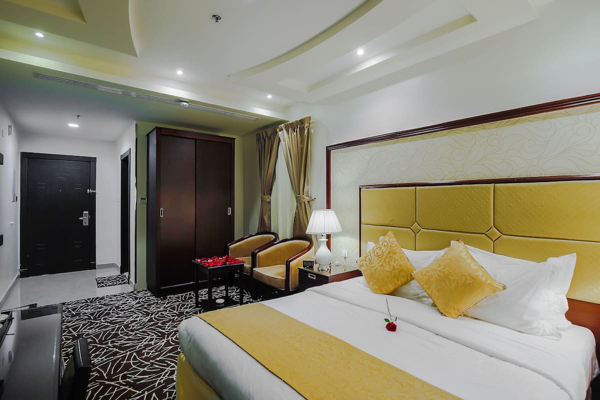 A hotel room with a large bed, a desk, a chair, and a wardrobe.