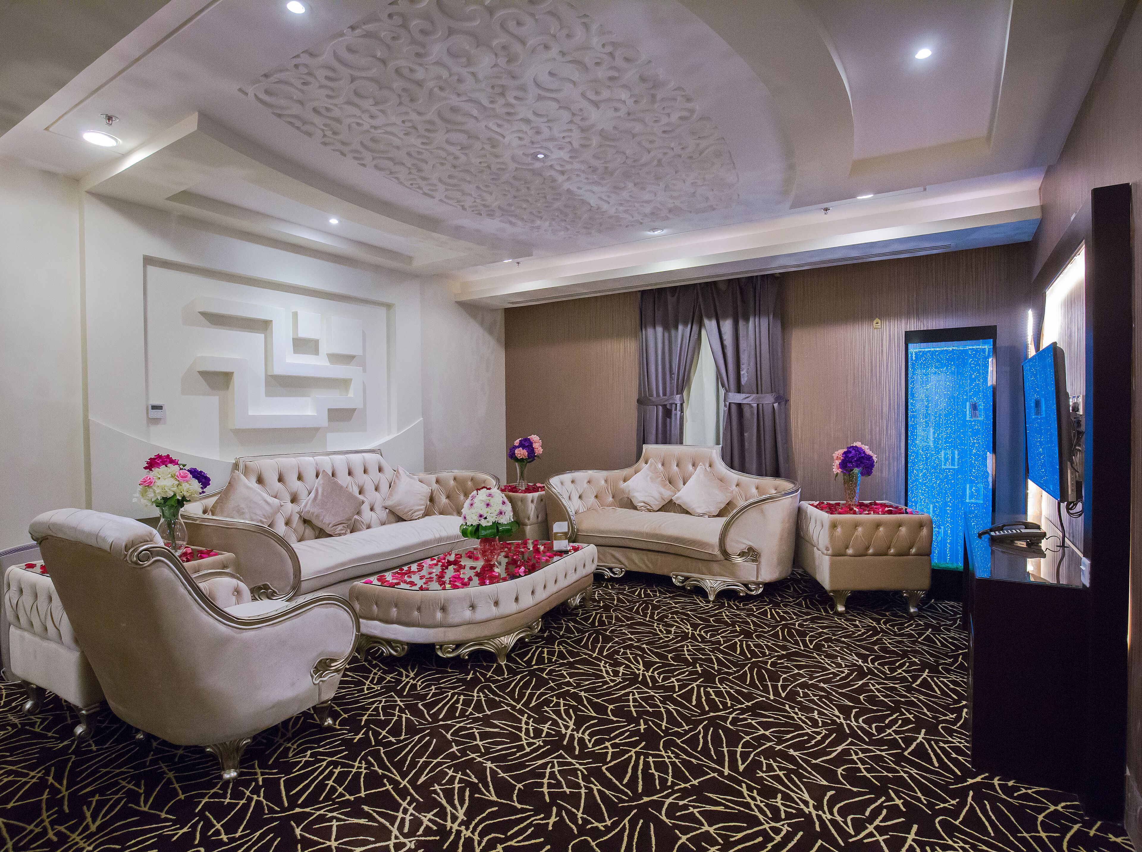 A luxurious living room with a patterned carpet, two sofas, a coffee table, and decorative flowers.