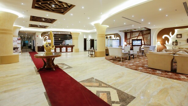 A spacious lobby with a red carpet, a reception desk, and a seating area with sofas and chairs.