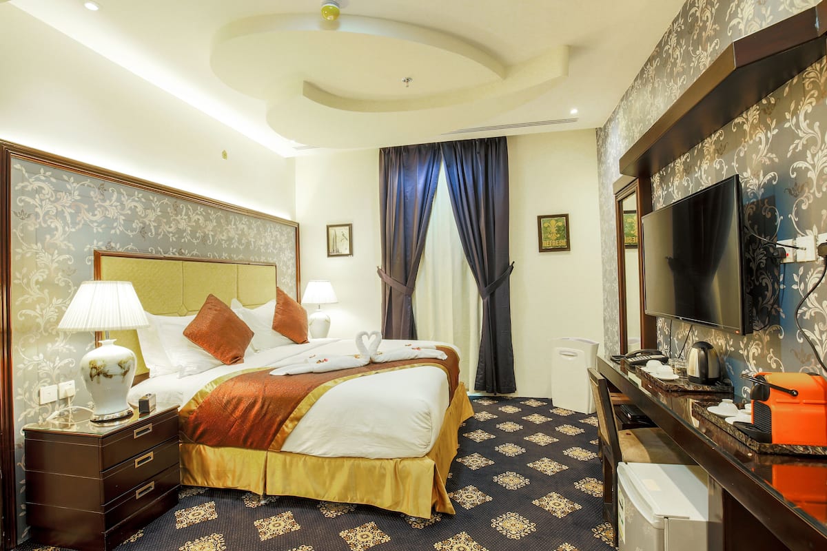 A hotel room with a large bed, a television, a desk with a coffee maker, and a minibar.