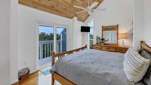 Een slaapkamer met een houten plafond, een bed, een dressoir, een spiegel en een televisie.