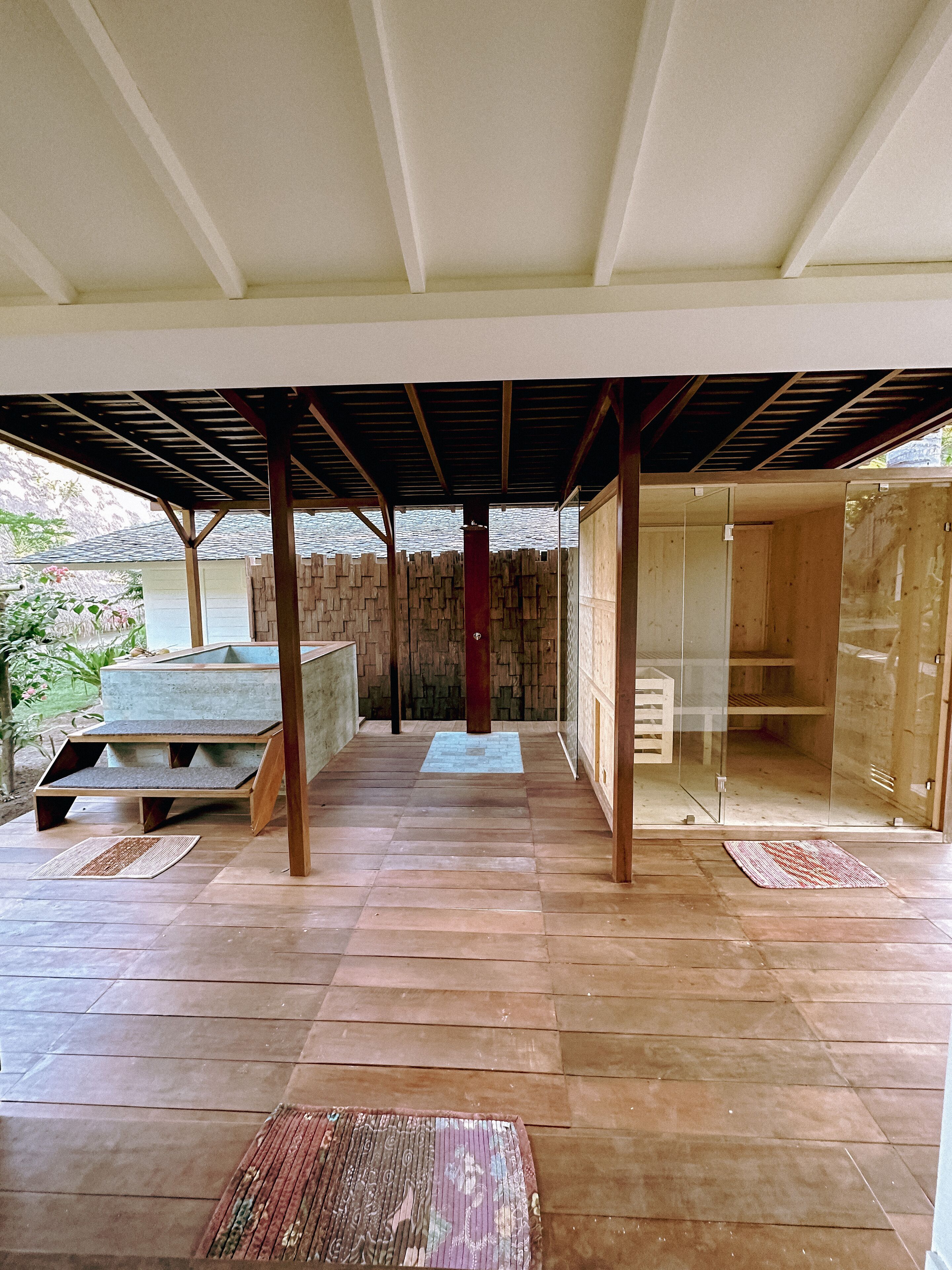 A covered outdoor area with a wooden floor, a central column, and glass walls.