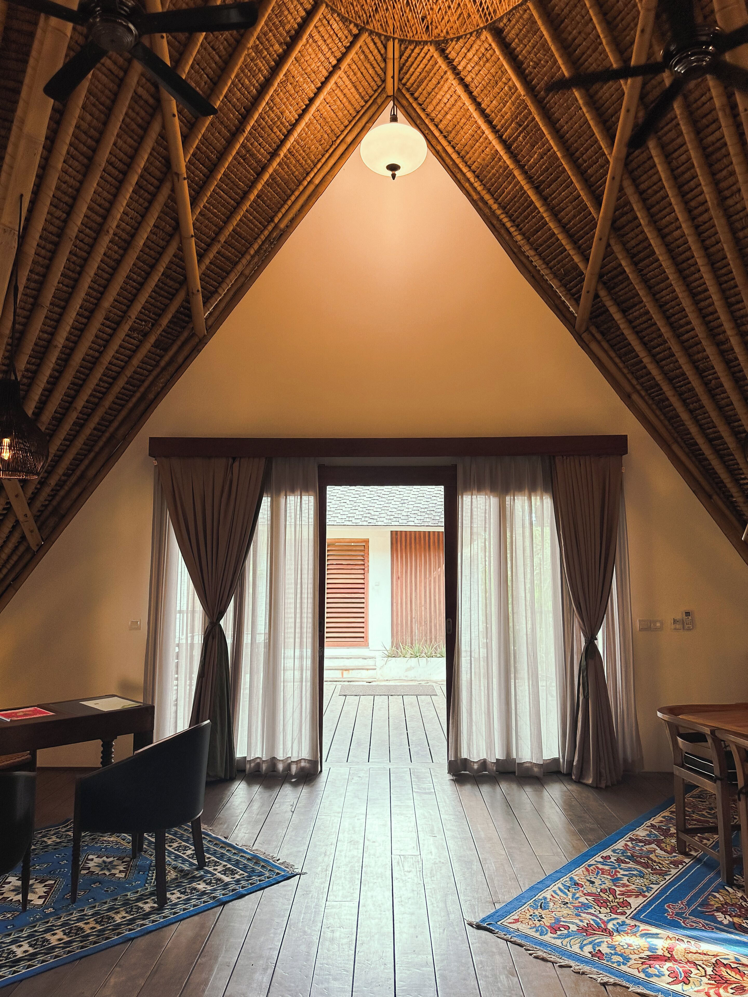 Ein Dachzimmer mit geneigter Decke, Holzboden, einem Tisch, einem Stuhl und Blick durch ein blickdichtes Fenster.
