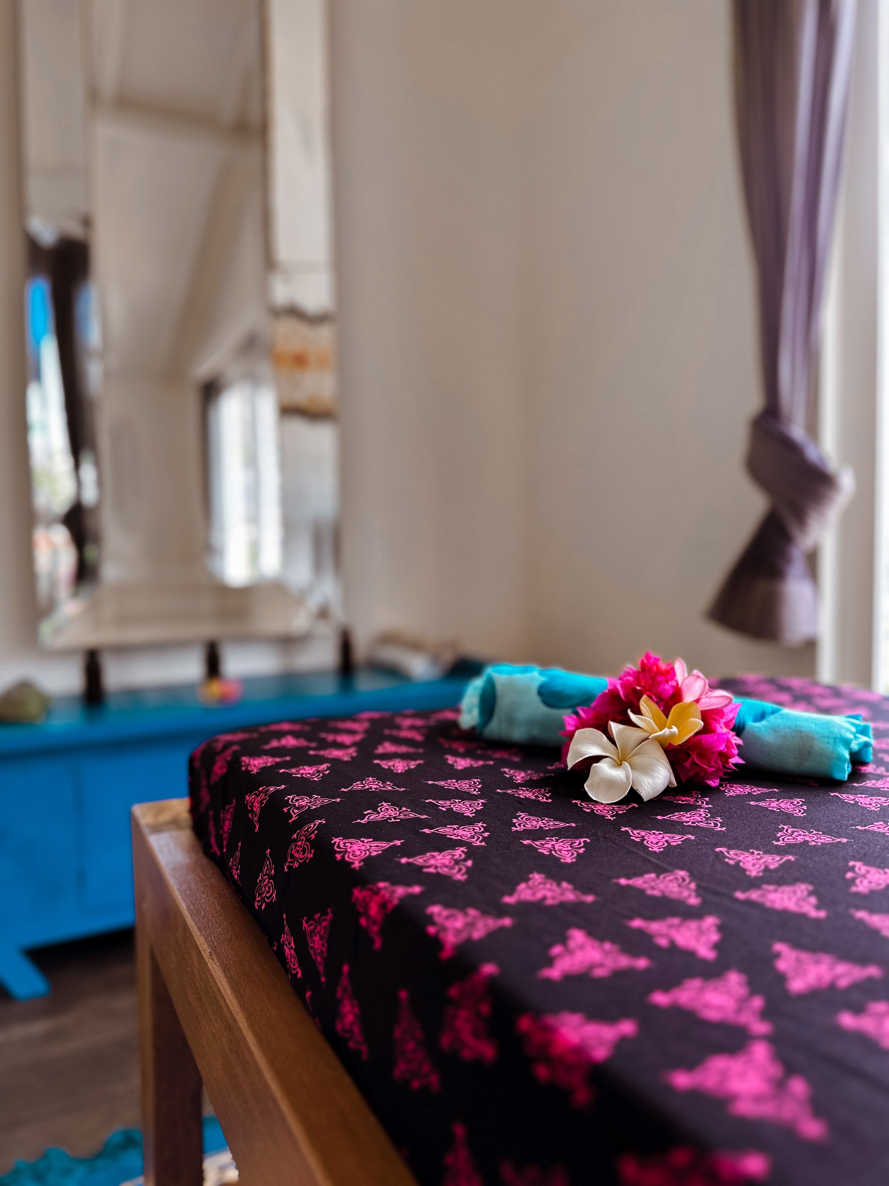 Una cama con una colcha estampada en negro y rosa, un cabecero de madera y una almohada azul.