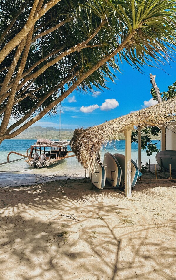A beach scene with a thatched roof structure, a boat, and a palm tree.