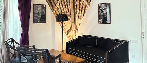 A room with a high ceiling, a black sofa, a wooden coffee table, a patterned rug, and a chair.