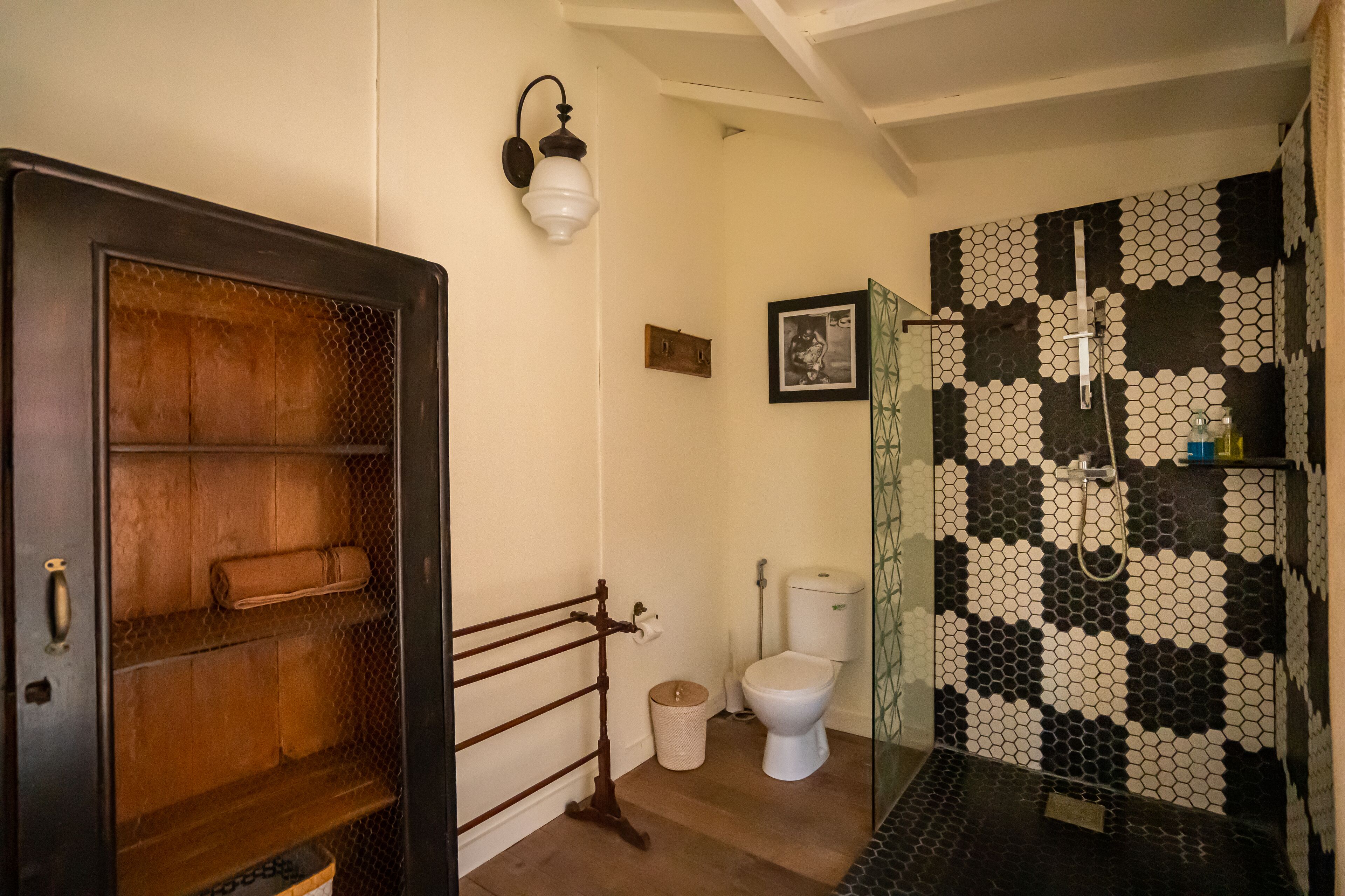 A bathroom with a wooden door, a white toilet, a black and white tiled shower area, and a wall-mounted light fixture.