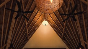 Une pièce mansardée avec un plafond en pente, des poutres apparentes, un luminaire suspendu, une table à manger et une vue sur l’extérieur à travers les rideaux.