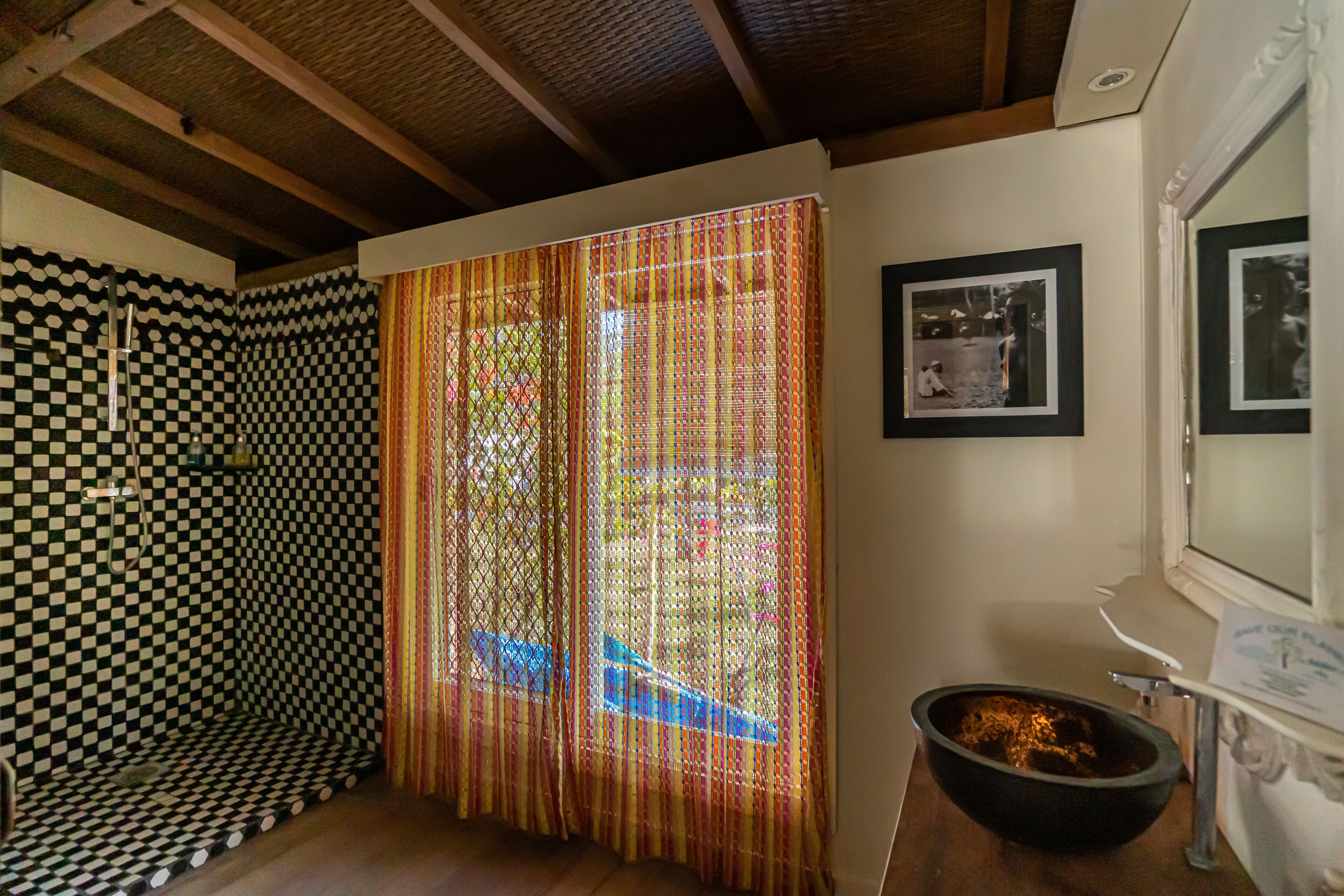 A room with a checkered wall, a patterned curtain, a framed picture, and a black bowl on a counter.