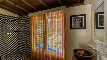 A room with a checkered wall, a patterned curtain, a framed picture, and a black bowl on a counter.