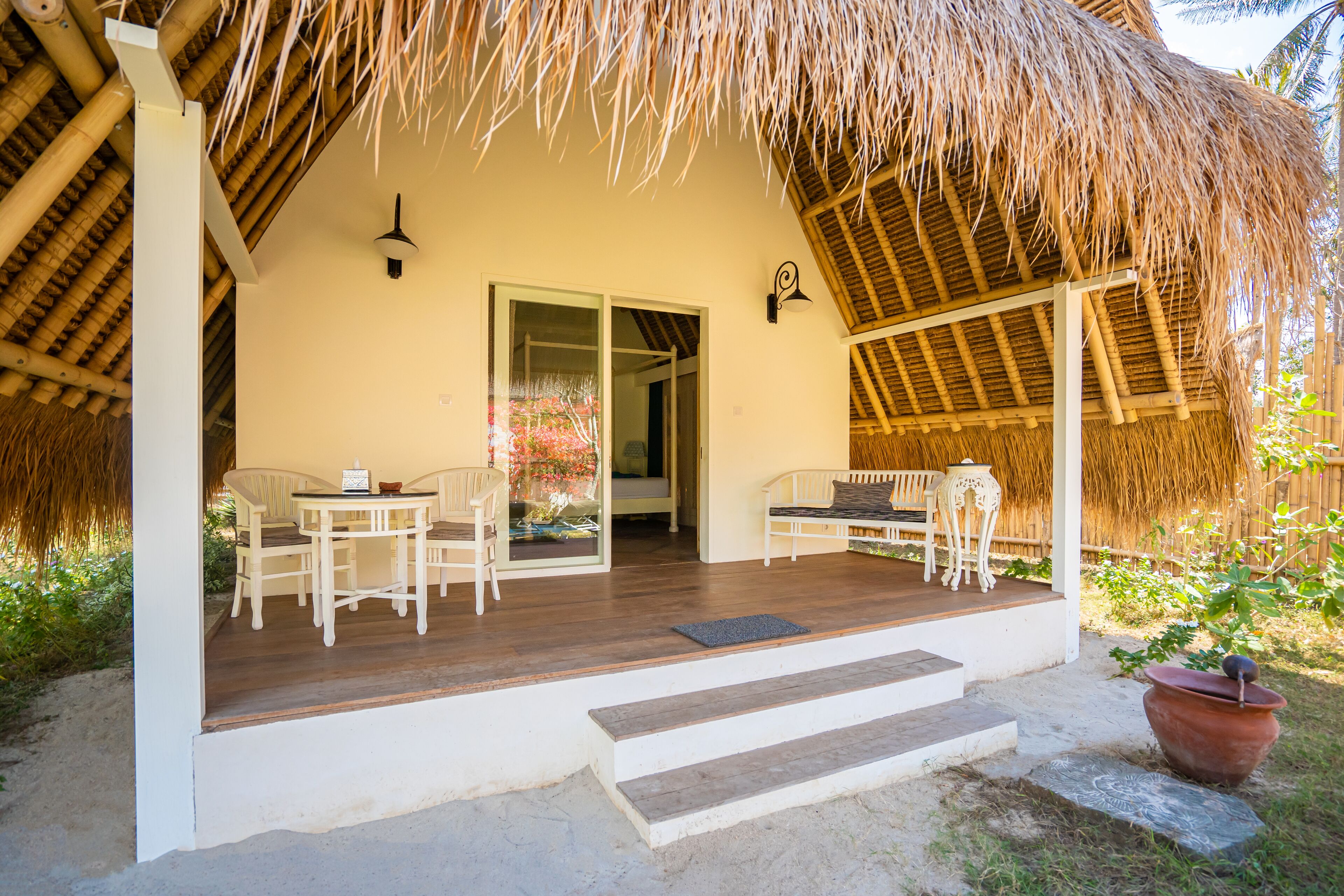 A covered outdoor seating area with a wooden deck, white furniture, and a thatched roof structure.
