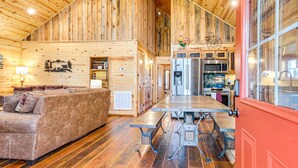 A spacious living area with a wooden ceiling, a sofa, a dining table, and a kitchen with modern appliances. - Hot Tub + Fire Pit: Dog-Friendly Cabin in Murphy! (Murphy)
