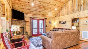 A log cabin interior with a stone fireplace, wooden floors, a red door, and a cozy seating area. - Hot Tub + Fire Pit: Dog-Friendly Cabin in Murphy! (Murphy)