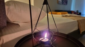 Eine Kerze in einem geometrischen Halter auf einem Nachttisch in einem Hotelzimmer.