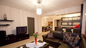 Ein modernes Wohnzimmer mit Fernseher, einer Couch, einem Couchtisch und einer Bar mit Regalen voller Flaschen.