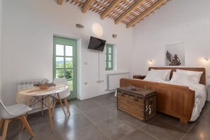 Une pièce comprenant un lit, une commode en bois, une table avec des chaises, un téléviseur fixé au mur et une porte verte.